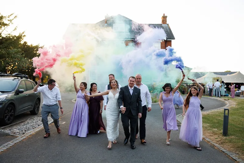 Wedding party celebrating with coloured smoke outside the teepee marquee at The Lodge, Duxford