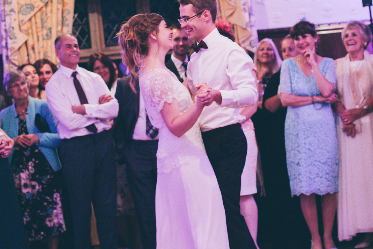 A bride and groom sharing their first dance while family and friends watch and smile around the floor