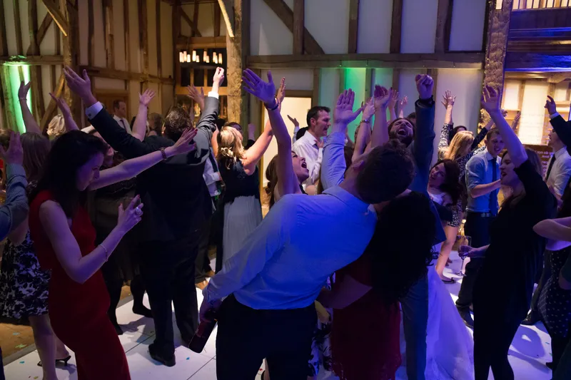 Wedding guests with their hands in the air on a packed dance floor in a timber-framed barn
