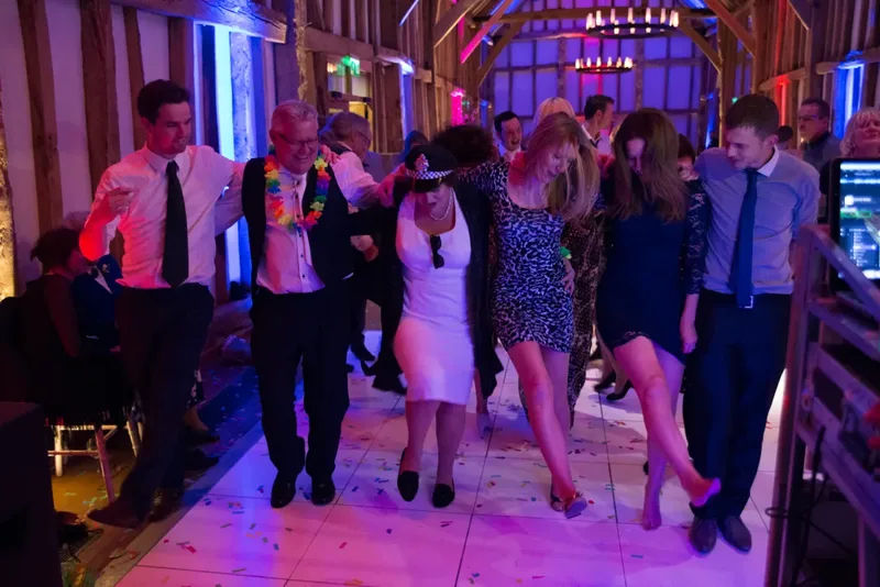 Wedding guests dancing together under pink and purple lights in a barn