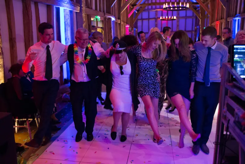 Wedding guests dancing together under pink and purple lights in a barn