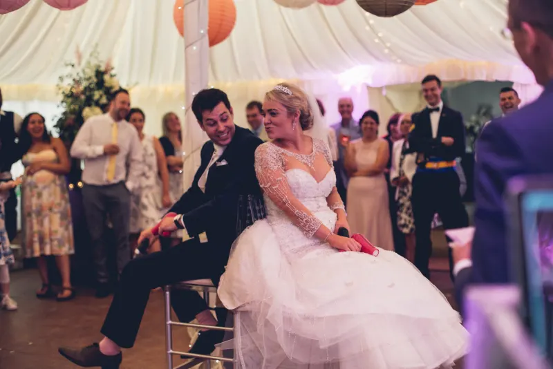 A bride and groom laughing together during a Mr and Mrs game as guests watch