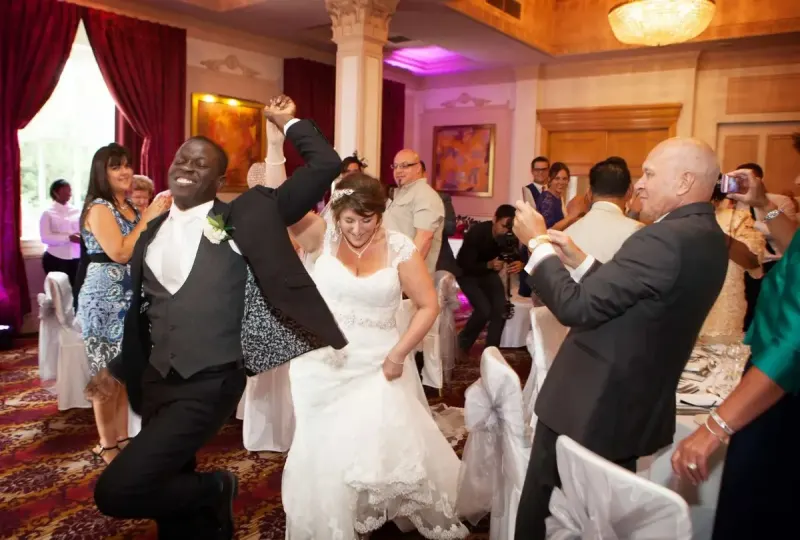 A bride and groom making a lively grand entrance into their reception as guests cheer