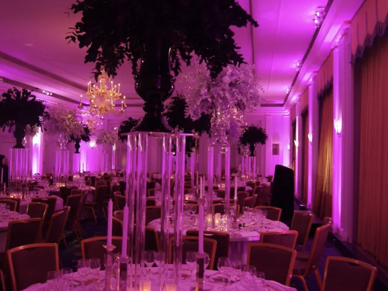 A wedding breakfast room lit with pink uplighting and tall floral centrepieces